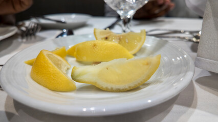 Close-up of lemon wedges on a white plate, elegantly arranged on a dining table.