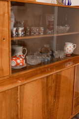 A collection of vintage glassware and ceramic items is displayed in a wooden cabinet. The warm light of the day highlights the craftsmanship of the pieces, creating an inviting atmosphere
