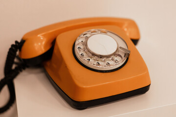 A bright orange rotary telephone is positioned on a white table, highlighting its retro design. This classic phone evokes nostalgia and showcases intricate craftsmanship common in earlier decades