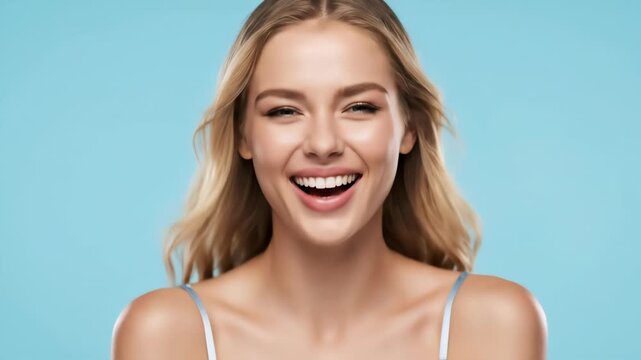 Close up of a cheerful blonde woman with head back laughing heartily against a solid blue backdrop. She is wearing a white top. Studio lit, warm lighting, bright.