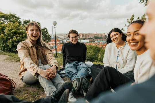 Portrait of smiling male and female friends spending leisure time with each other sitting on hill