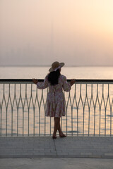 Fototapeta premium Silhouette of girl admiring Dubai city skyline at golden hour, scenic view from Dubai Creek harbor in winter - Vertical stock photo