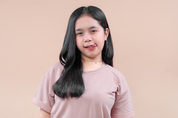 Fototapeta premium Asian woman in casual modern outfit posing with playful expression, slightly sticking out her tongue, showing charm, confidence, and youthful energy.