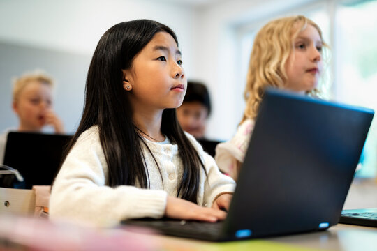 Female student with laptop sitting next to friend at desk in classroom