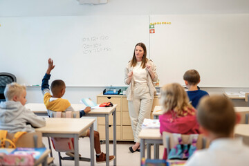 Female teacher teaching mathematics to group of elementary students sitting at desk in classroom