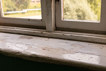 Peeling paint and an aged window sill highlight the deteriorating condition of an old building in an urban area, reflecting years of neglect and lack of maintenance