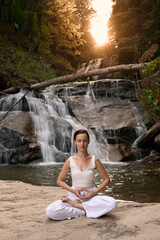Young woman sitting in lotus pose under tropical waterfall meditating with calm strength and mindfulness fully connected to nature energy tranquility and inner balance