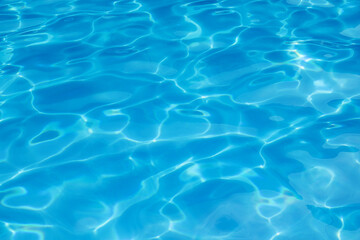 Water in swimming pool rippled water detail background. Water in swimming pool with sun reflection. Blue swimming pool rippled water detail.