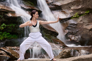 woman performing slow tai chi movements near a waterfall and river at sunset capturing harmony balance and fitness in nature