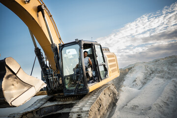 Construction worker driving excavator at quarry in open pit mine