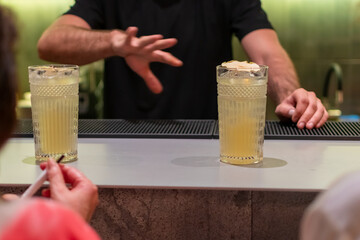 Final steps of making a drink with bartender stirring two cocktails in textured glasses and then presenting finished drink to a customer