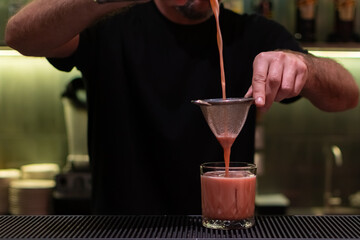 Final steps of making a cocktail. Bartender strains the finished drink through a sieve into a glass