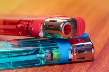 Two red and blue plastic lighters are resting on a wooden surface , photographed in close-up