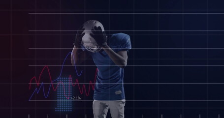 Clutching helmet to head, football player wearing blue jersey standing in studio, with data graphs