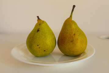 Pair of ripe pears displayed on a clean white plate against a neutral background. The simple composition conveys freshness, healthy eating, minimalism, and seasonal nutrition in food photography.