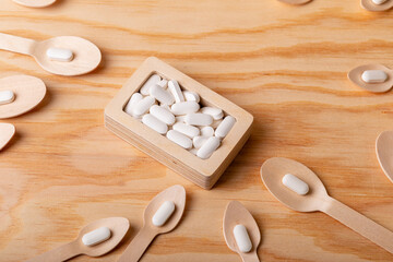 White vitamin pills in wooden box and wooden spoons on wooden desk from above on wooden background....