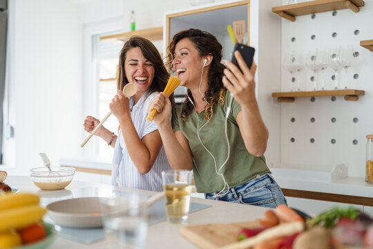 Young Women Enjoy Cooking and Singing Together in a Bright Modern Kitchen Setting