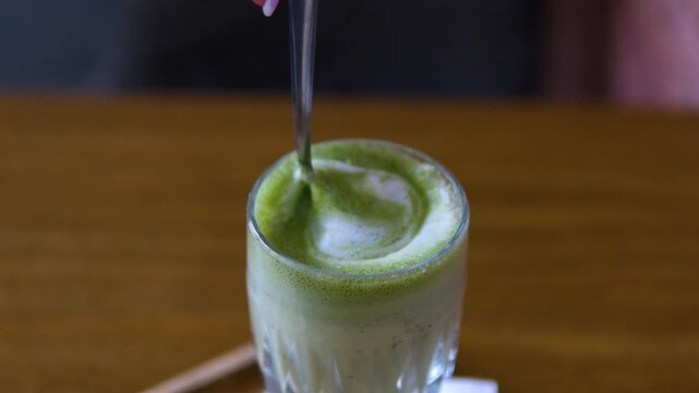 mix with a spoon Matcha green tea latte with ice and tapioca pearls. Matcha latte being stirred with a drinking straw.