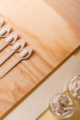 White tablets in wooden spoon and glass bowls with vitamins from above on a wooden desk. Meds, vitamins and minerals, dietary supplements. Healthy lifestyle. Top view.