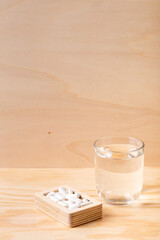 Glass of water and white pills in wooden box on wooden desk on wooden background. Vitamins, minerals and food supplements to protect your health and immune system. White tablets.