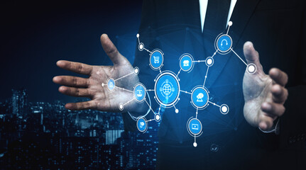 A businessman stands against a cityscape at night, presenting a digital network interface, symbolizing technology, innovation, and data sharing in modern business. Tessel