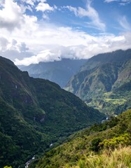 Fototapeta premium Lush green valley nestled between towering mountains under a vibrant blue sky dotted with fluffy white clouds.