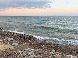 The sea reflects soft evening light under cloudy sky with distant horizon line. Calm waves, marine ecology and coastal landscape in seasonal outdoor environment.