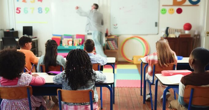 School, kids and question with teacher in classroom for education, studying and lesson. Learning, child development and growth with students and man in Montessori for hands raised and support