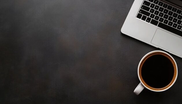 A laptop and a cup of black coffee sit on a dark gray textured surface; the scene is viewed from above.