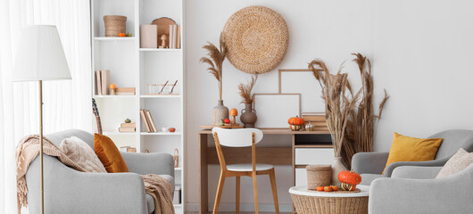 Interior of light living room with autumn decor, sofa and armchairs