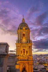 Obraz premium Tower of Málaga Cathedral at blue hour, with magenta sky and the illuminated church top during sunset, highlighting historic architecture.