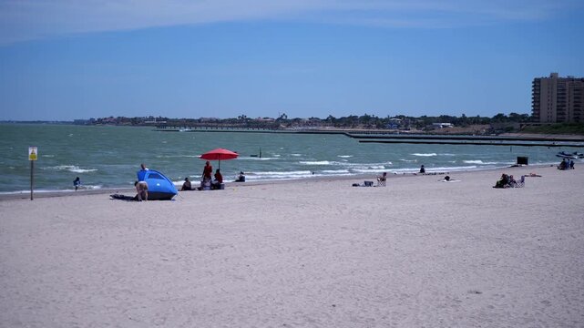 Wide shot of beachgoers relaxing along a sandy bayfront during summer. Great for vacation, leisure, or coastal living themes.