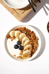 Greek Yogurt with Homemade Granola, Fresh Blueberries and Banana on Kitchen Table.	