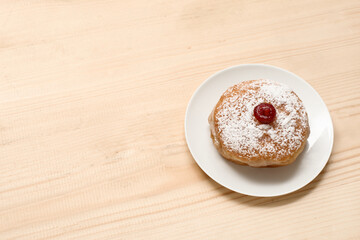 Plate with tasty donut for Hanukkah celebration on wooden background