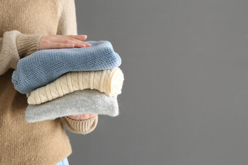 Woman holding stack of different stylish sweaters on grey background