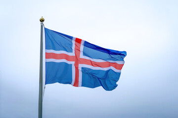 The blue, red, and white national flag of Iceland captured mid-wave against a cloudy sky background