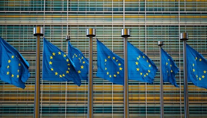 The image shows multiple EU flags fluttering on flagpoles against a backdrop of a contemporary glass and metal structure.