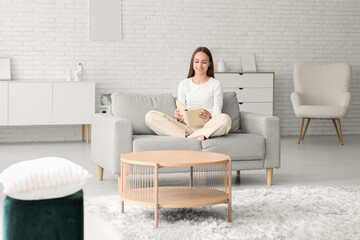 Young pretty woman reading book on cozy couch at home