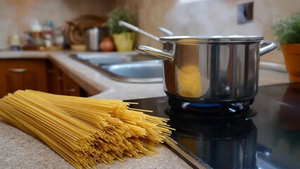 Close-up of a pack of dry spaghetti on a kitchen countertop. In the background is a pot of boiling water. Preparing to cook dinner. Perfect for food, cooking, and healthy eating content. - Powered by Adobe