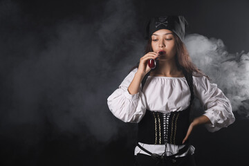 Beautiful young Asian woman dressed as pirate with smoking pipe on black background