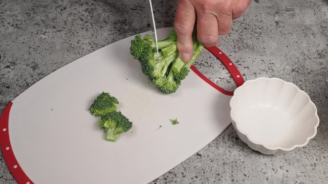 Cutting florettes off a stalk of broccoli on a white cutting board
