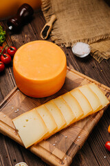 Whole cheese wheel with slices on rustic board, served with herbs and vegetables