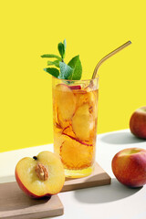 Glass of tasty iced tea with mint and peaches on beige table against yellow background
