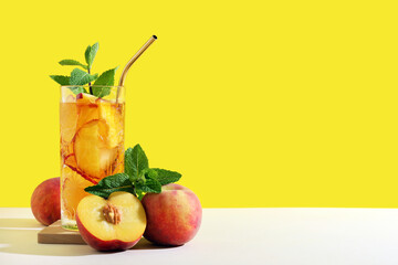 Glass of tasty iced tea with mint and peaches on beige table against yellow background