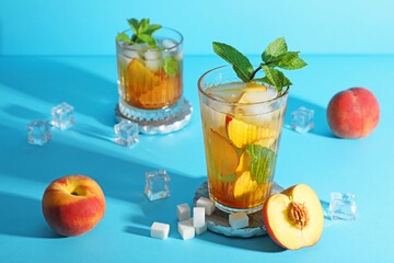 Glasses of tasty peach iced tea on blue background, closeup