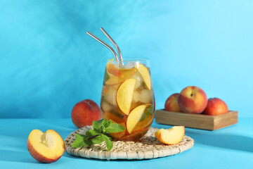 Glass of tasty peach iced tea and wicker mat on blue background, closeup