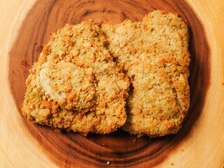 Breaded chicken breast fillet on a wooden board. Classic poultry product. Uncooked meat covered with golden breadcrumbs.