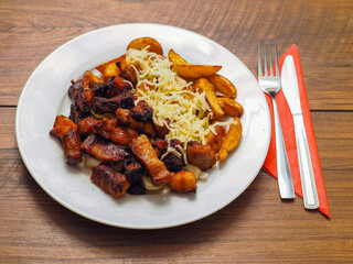 A plate of food with mini pork belly slices and potatoes and cheese and a fork and knife on a table. Scene is casual and inviting. Tasty simple food.