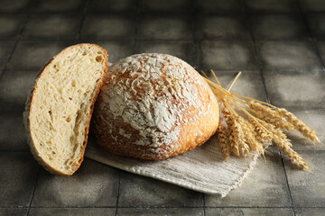 Napkin with cut loaf of fresh bread and wheat on grey tiled table