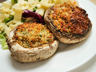 A plate of food with a fork and knife on a wooden table. The plate has a fresh salad with cheese and two fancy posh stuffed mushroom patties. Simple tasty meal.